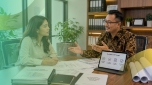 Foto suasana konsultasi antara seorang wanita dan seorang pria berkemeja batik yang sedang menjelaskan alur pengurusan Sertifikat Laik Fungsi (SLF) menggunakan tablet di ruang kantor.