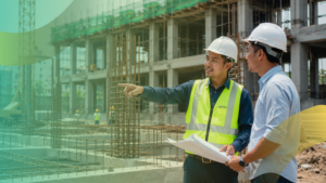 Dua auditor teknis bangunan menggunakan helm proyek sedang melakukan inspeksi lapangan untuk pemeriksaan kelaikan fungsi struktur beton gedung